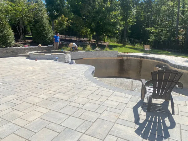Large paver patio with curved seat wall around a pool under construction