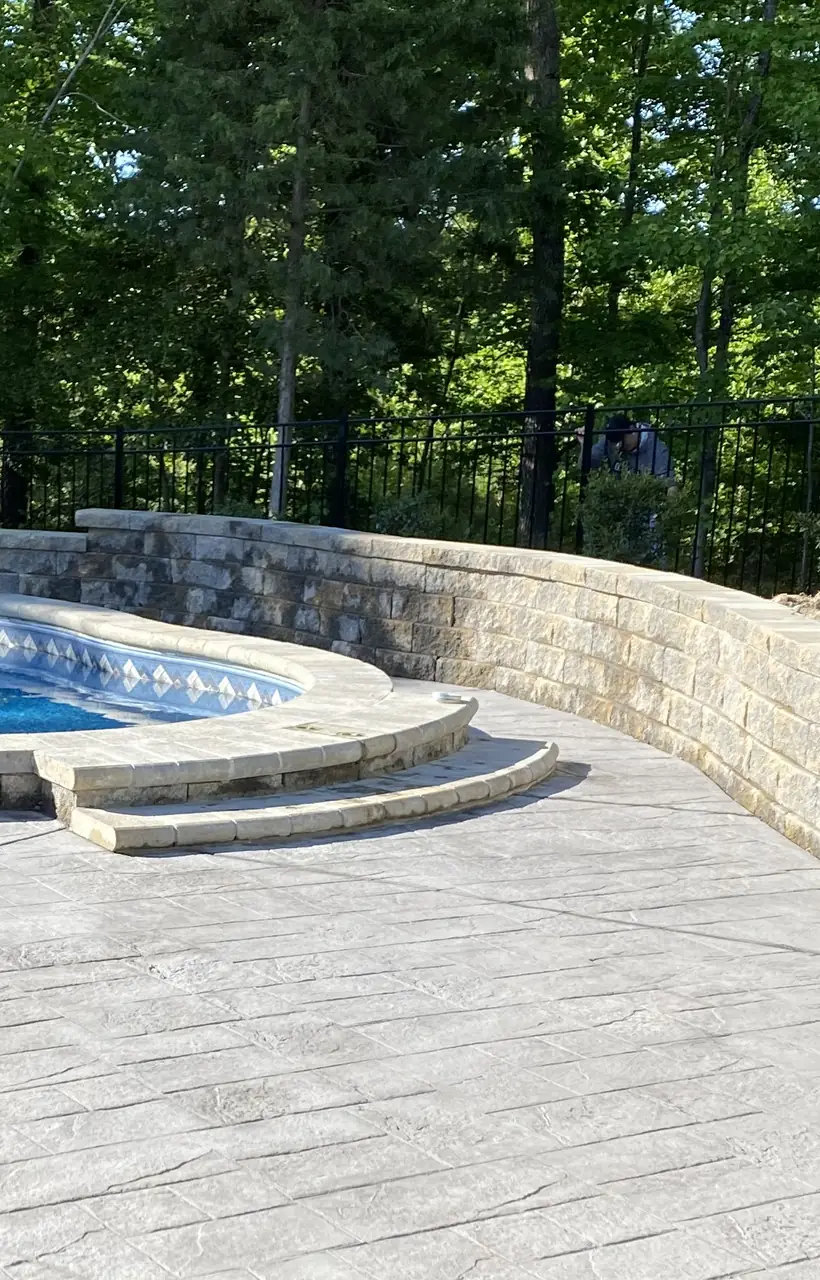 Freeform pool with a curved stone seat wall and a stamped concrete deck, built by Barcenas and Sons