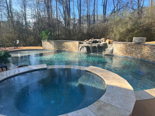 Pool with a natural stone waterfall feature and travertine coping