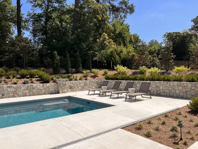 Pool with a stone retaining wall and a paved deck
